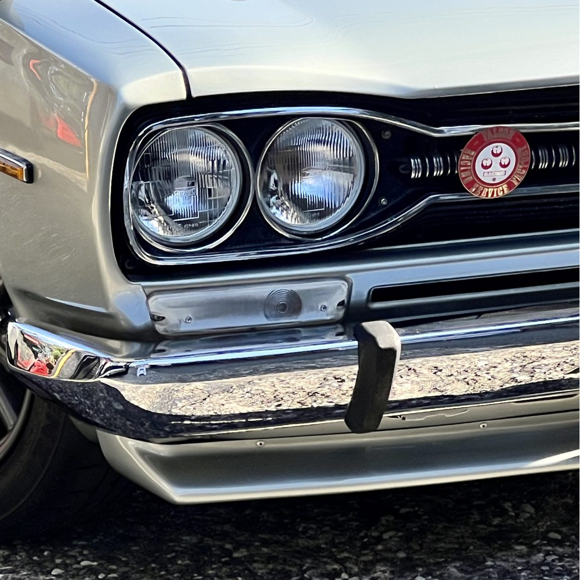 Close-up of a classic car's front grille and headlight on a gravel surface