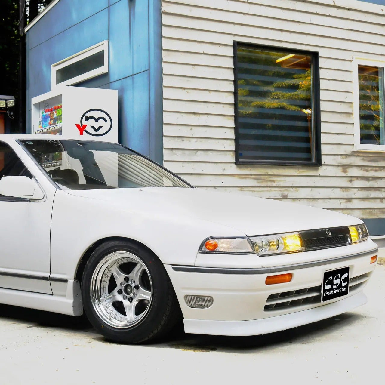 White car parked in front of a building with a logo on the wall.