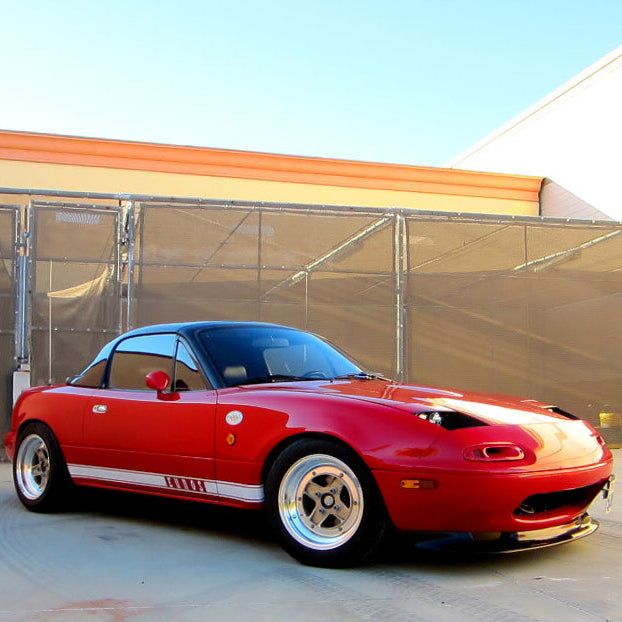 Red sports car with white stripes parked in front of a building