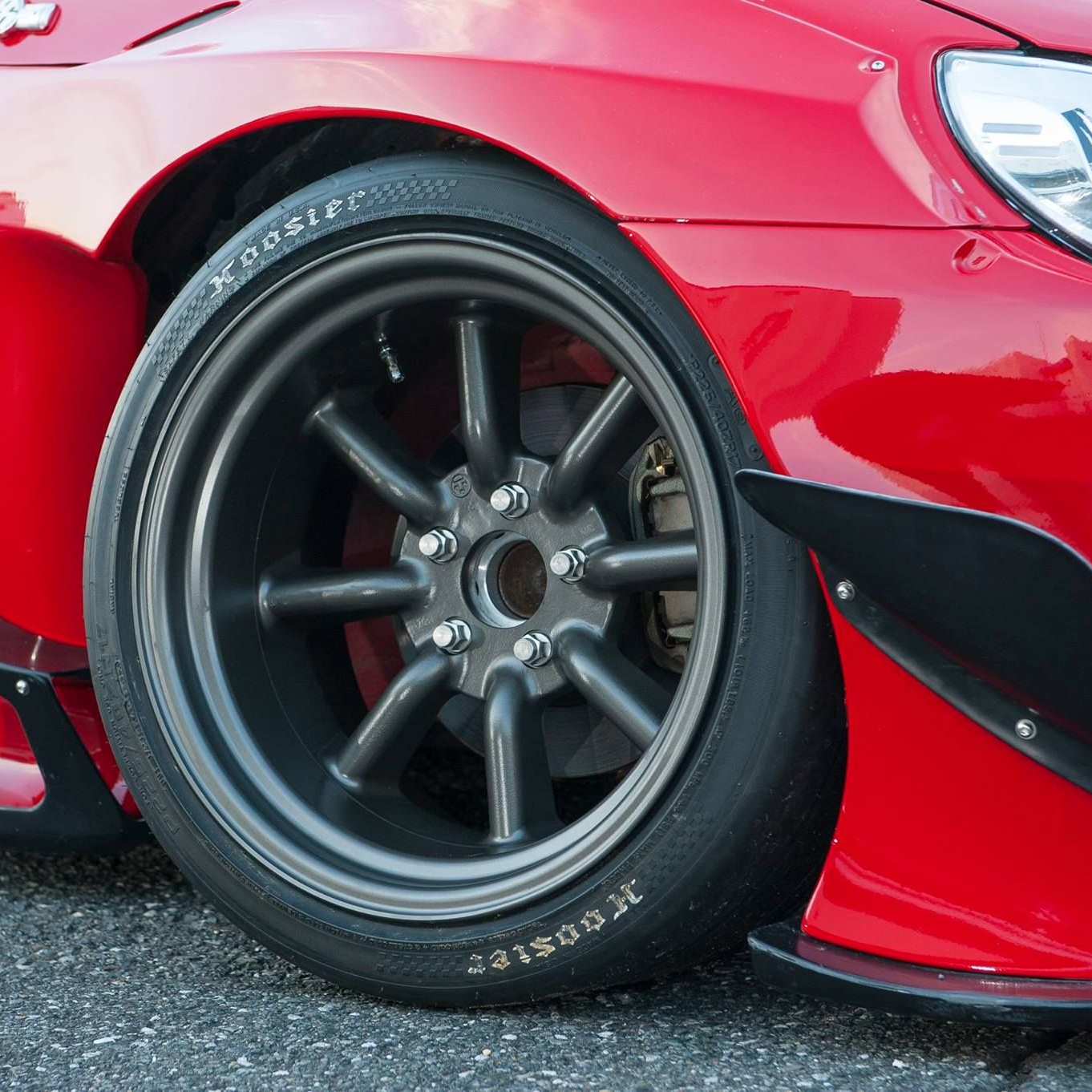 Close-up of a red car with a black wheel and tire on a road.