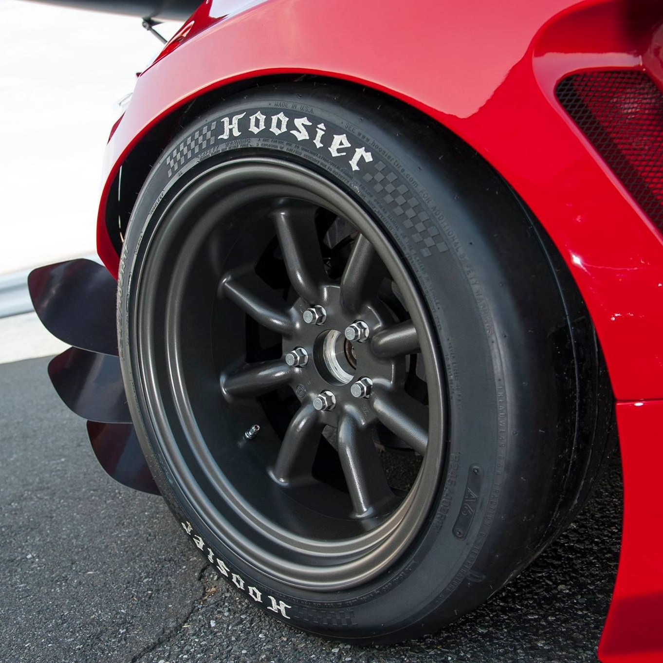 Close-up of a red car's wheel with 'Hoosier' branding on a track.